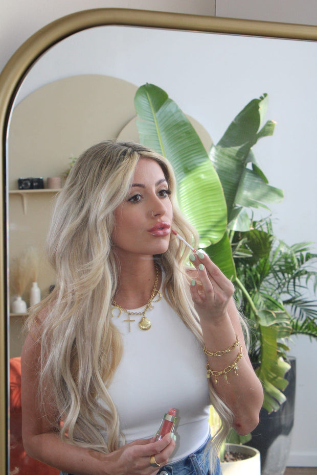 Woman wearing several charm bracelets while looking in mirror fixing makeup.